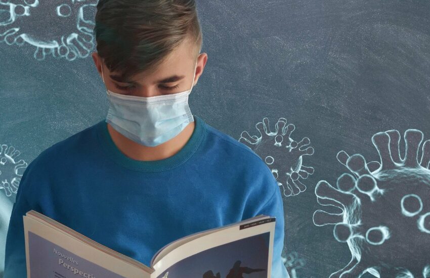 Ein Schüler steht vor der Tafel mit Maske und Viren